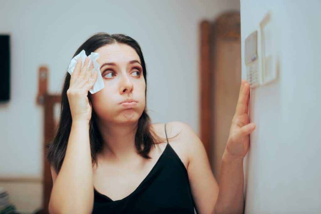 Woman checks for thermostat issues in uncomfortably hot home during the winter